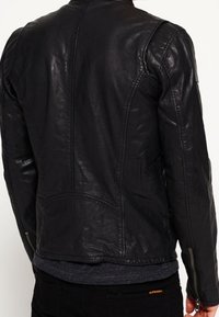 Giacca in pelle nera con un design aderente, texture liscia e dettagli di cucitura sottili. Include zip sulle maniche e tasche laterali.