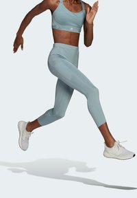 Jasnoniebieski zestaw sportowy z biustonoszem sportowym z regulowanymi ramiączkami i legginsami o wysokim stanie, oba z gładkiego i gładkiego materiału, w połączeniu z białymi trampkami.