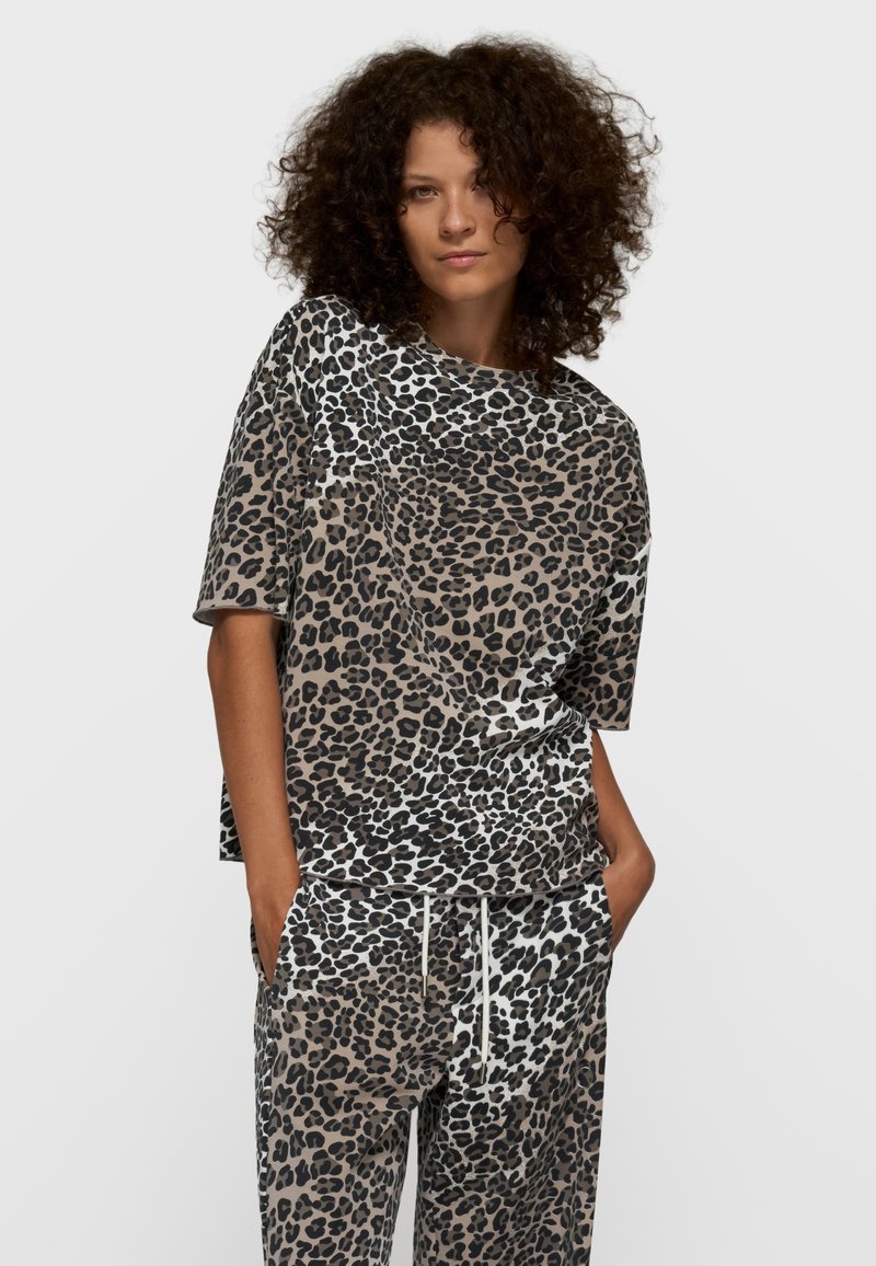 Ensemble de vêtements d'intérieur à imprimé léopard en marron, noir et blanc. Haut à manches courtes avec coupe ample et fentes latérales ; pantalon assorti avec cordon de serrage.