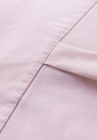 Lichtroze stof met een gladde textuur en zichtbare stiksels. Heeft een vouw en naad, die de lichte kwaliteit van het materiaal benadrukken.