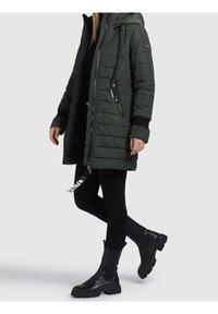 Zielona pikowana długa kurtka z kapturem, czarne akcenty metalowe i zamek błyskawiczny. Połączona z czarnymi dopasowanymi spodniami i botkami za kostkę.