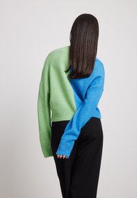 Suéter con diseño dividido, con un lado en verde claro y el otro en azul brillante, hecho de un material de punto texturizado.