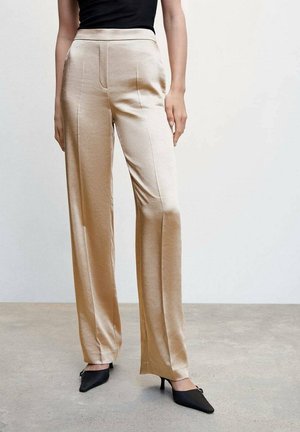 Woman wearing beige wide-leg satin pants with a high waist, paired with black pointed-toe kitten heels and a black sleeveless top.