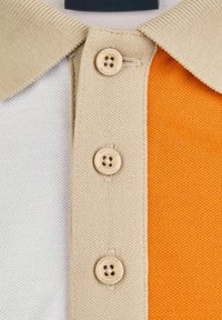 Polo à manches courtes avec un col beige et trois boutons, doté de blocs de couleur blanche, beige et orange en tissu texturé.