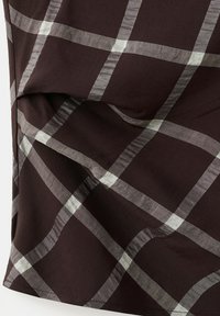 Tissu marron foncé avec un grand motif à carreaux gris clair en damier et des coutures visibles le long du bord.