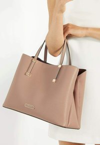 Roze leren tote bag met gepolijste gouden hardware, vlakke gestructureerde vorm en dubbele handvatten, met een logo-detail aan de voorkant.