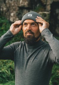 Gray knit beanie with a logo tag, worn by a man in a matching long-sleeve base layer top. The fabric appears textured and fitted.