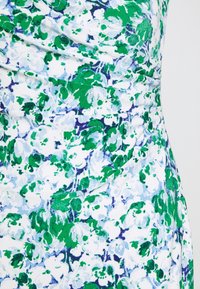 Blommönstrad tyg med gröna, vita och blå nyanser samt mjuk textur. Designen inkluderar en rynkad midja med ett flödande fall.