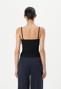 Schwarzes, geripptes Tanktop mit dünnen Trägern, tailliert. Der Rücken zeigt ein schlichtes Design, kombiniert mit marineblauen, weit geschnittenen Hosen.