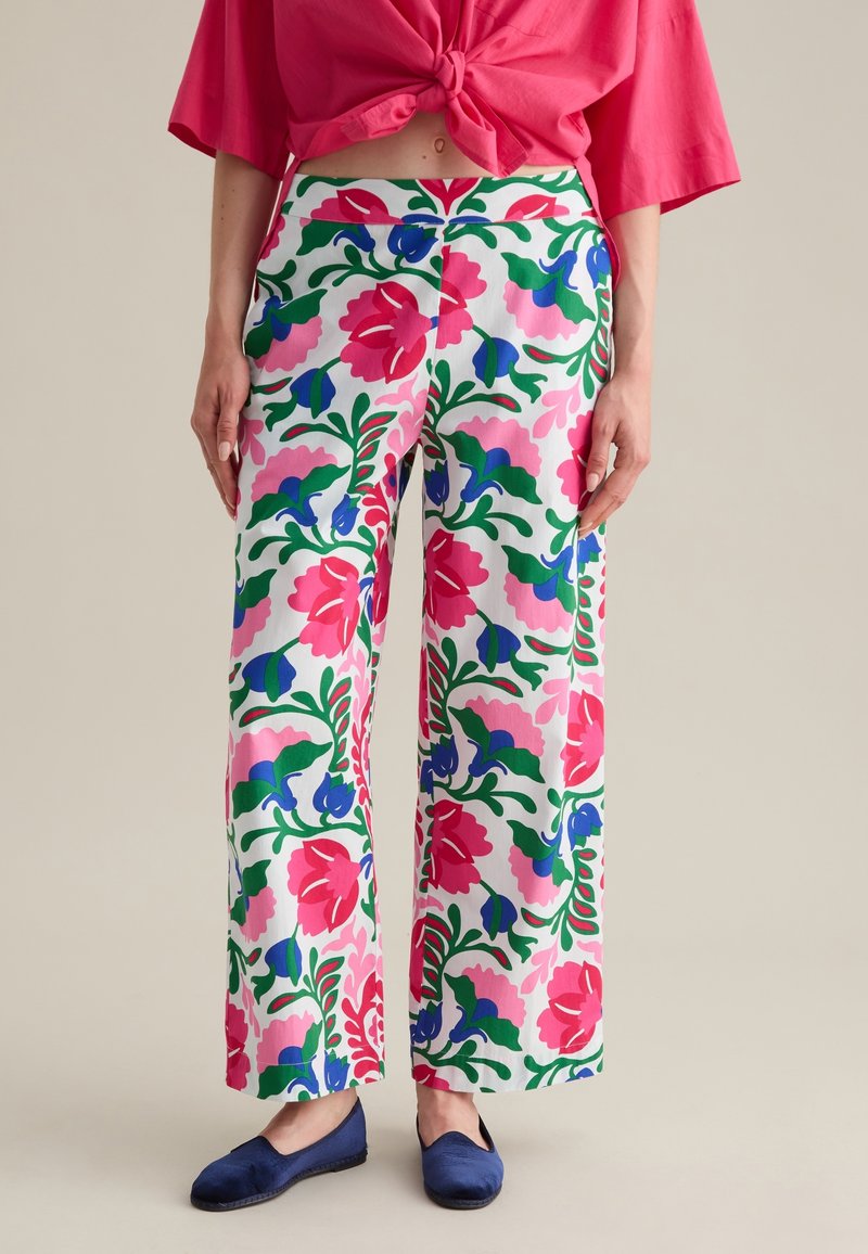 Un pantalon large à fleurs présente un fond blanc avec des motifs vibrants en rose, bleu et vert. Fabriqué en tissu léger, il offre une coupe décontractée.