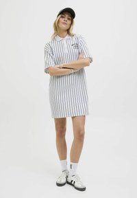 Robe polo à rayures blanches et noires avec des manches courtes. Avec un col et un logo sur la poitrine. Associée à des chaussettes blanches et des baskets.