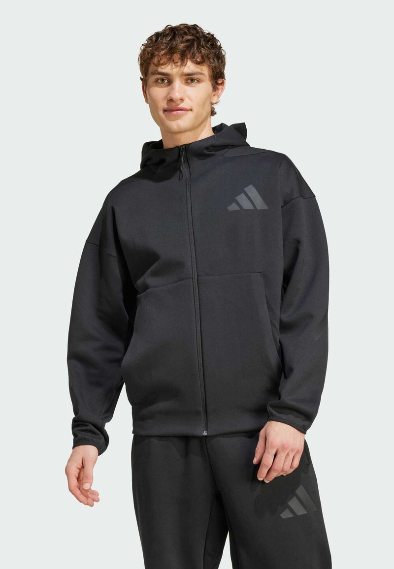 Sweatshirt preto com fecho éclair e capuz, apresentando um logótipo Adidas preto mate no peito e um bolso canguru. Tecido suave e ajuste descontraído.
