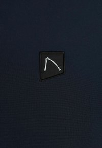 Tessuto blu navy con una superficie liscia, presenta una toppa nera cucita con un design geometrico bianco nell'angolo inferiore.