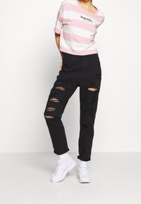 Pruhované růžové a bílé zkrácené tričko s logem "Superdry", spárované s černými vybledlými džíny s velkými trhlinami a bílými teniskami.