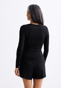 Zwarte lange mouwen top van zachte stof, aansluitend design, met een ronde halslijn. Gecombineerd met zwarte shorts, die een gladde textuur tonen.