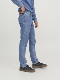 Jeans de mezclilla azul con corte ajustado, con una cintura de altura media, cinco bolsillos y detalles de costura sutiles, combinados con zapatillas negras.