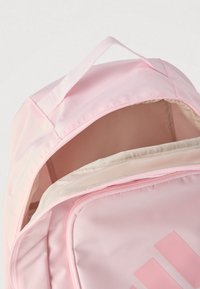 Ροζ σακίδιο από συνθετικό ύφασμα με πάνω λαβή και ανοιχτό φερμουάρ που δείχνει εσωτερικό σε μπεζ χρώμα. Διαθέτει εμφανές ροζ λογότυπο στο μπροστινό μέρος.