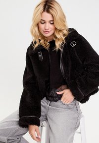 Schwarze Schafslederjacke mit strukturiertem Finish, mit Lederakzenten, übergroßer Passform und durchgehendem Reißverschluss. Das Modell trägt graue Jeans.