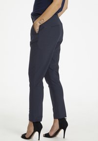 Navy pantalon met een slim fit, zijzakken en een gestroomlijnd ontwerp. Gecombineerd met zwarte open-toe hoge hakken. Soepele stof textuur.