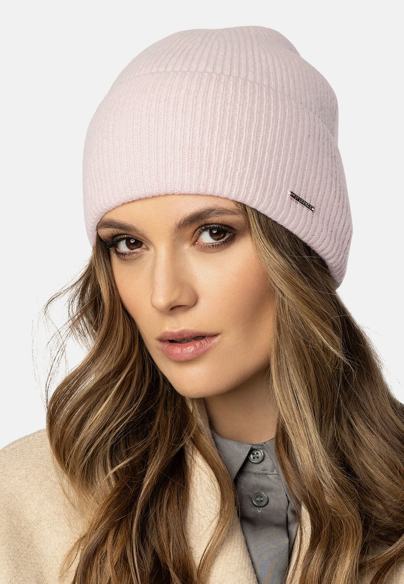 Bonnet côtelé rose clair avec un revers et une petite étiquette noire sur le côté. Texture douce et ajustement confortable.