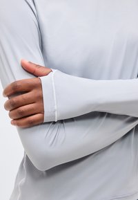 Inimene, kes kannab heledat halli pika varrukaga särki pöidlalõhedega, ristab käed ja keskendub vasakule käsivarrele ja käele.