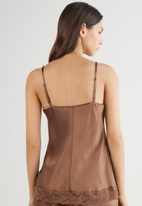 Bruine satijnen camisole met verstelbare bandjes, voorzien van kantafwerking aan de zoom en een gladde, glanzende textuur. Achteraanzicht weergegeven.