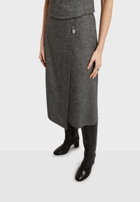 Siva suknja u riblju kost s oblikom omote, napravljena od teksturiranog materijala, uparena s crnim kožnim čizmama do bedrа. Suptilni detalj od metalnog hardvera.