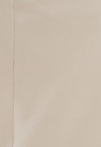 Vaaleanbeige kangas, jossa on sileä texture ja hieno kudonta. Hieman kiiltävä pinta ja näkyvä yksittäinen pystysauma. Ei selviä kuvioita tai tarvikkeita.