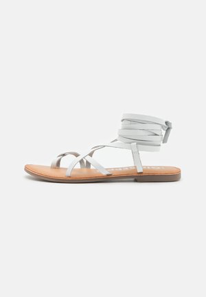 Sandali gladiatore bianchi in pelle con molteplici cinghie incrociate e design della caviglia avvolto. Presentano una suola tan e uno stile minimalista.