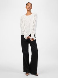 White blouse with diamond cutout patterns, long sleeves with flared cuffs, paired with black wide-leg pants and patterned open-toe shoes.