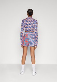 Pitkähihainen paita, jossa on kuviollinen sininen, vaaleanpunainen ja kerma väri sekä verkko-ominaisuus, yhdistettynä vastaaviin shortseihin, joissa on kukkakuosiset kirkkaat värit.