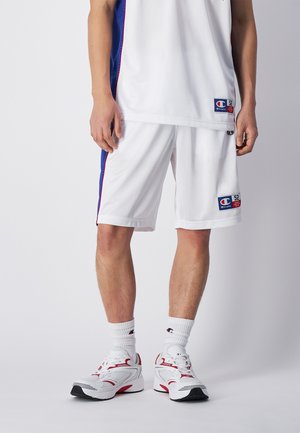 Pantalones cortos deportivos blancos con paneles laterales azules y detalles rojos, hechos de una tela suave. Llevados con una parte superior blanca a juego y zapatillas blancas.