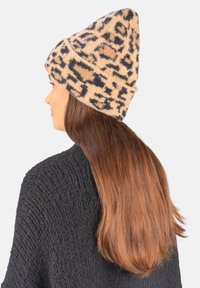 Knit beanie in beige with a black animal print pattern. Pointed top and soft texture, paired with a dark sweater.