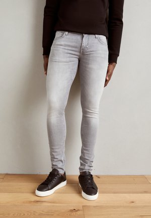 Jeans skinny grises con un acabado desgastado, que cuentan con un diseño clásico de cinco bolsillos y herrajes metálicos. Combinados con zapatillas negras.