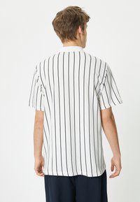 Valkoisella raidallisella T-paidalla on tummansiniset pystysuorat raidat, lyhyet hihat ja suora leikkaus. Kangas vaikuttaa sileältä ja kevyeltä.