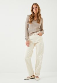 Beige ribbed pitkähihaine paita, jossa on vetoketjukaulus, yhdistettynä vaaleanbeigeihin leveälahkeisiin housuihin. Pehmeä texture, suora leikkaus, hienovarainen ommeltyö, matalat kengät.