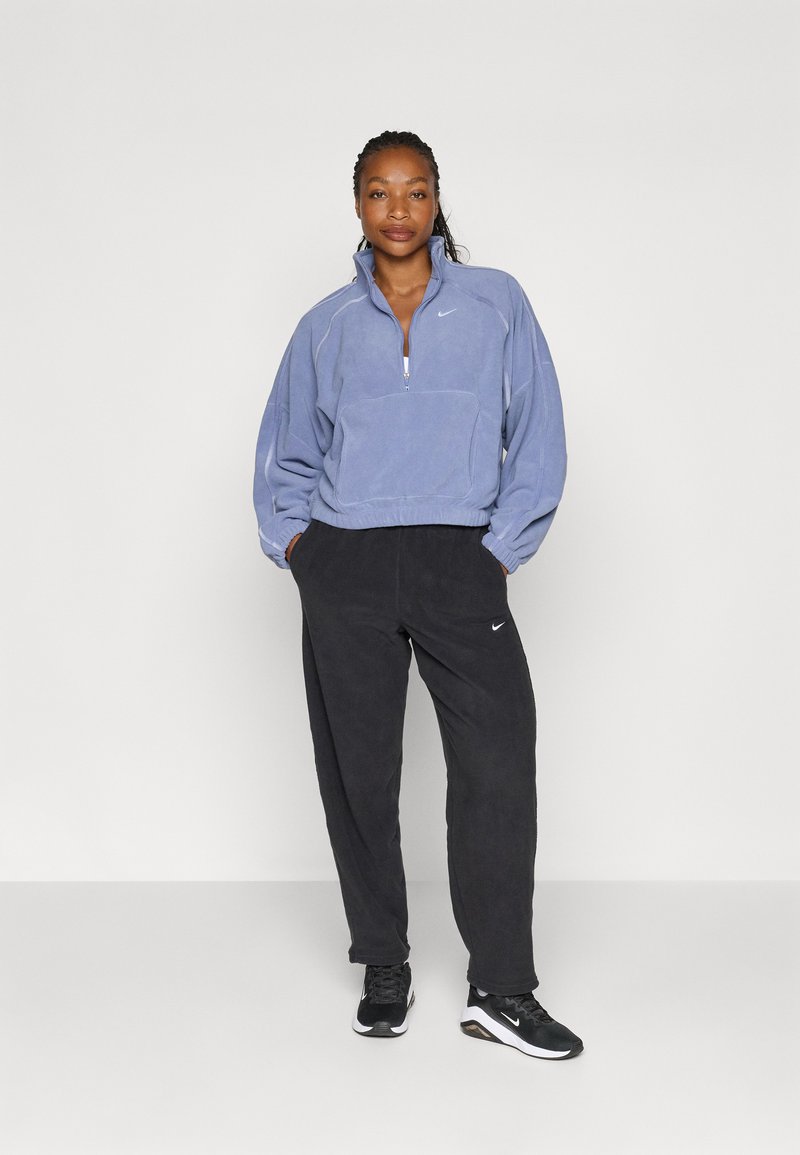 Lila Fleece-Halbzipper-Pullover mit Fronttasche, kombiniert mit schwarzen Fleecehosen, beide mit einem Nike-Logo. Schwarze Sportschuhe.