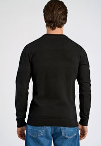 Czarny sweter z teksturowymi poziomymi paskami, z prążkowanymi mankietami i okrągłym dekoltem. Noszony z niebieskimi dżinsami, prezentując swobodny styl.