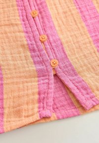 Camisa a rayas en colores naranja y rosa, hecha de tejido texturizado con cinco botones naranjas a lo largo de la tapeta y detalles de costura en contraste.