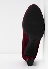 Chaussure femme en daim bordeaux à talon bas, vue de la semelle avec semelle et talon noirs, taille 37, nom de marque "Unisa" visible.