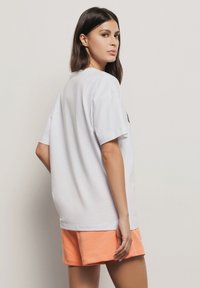 T-shirt bianco in cotone con maniche corte, collo a giro e vestibilità rilassata, abbinato a pantaloni corti arancioni. Design minimalista, senza grafiche o motivi.