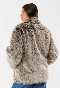 Cappotto in finta pelliccia beige con una texture soffice, vestibilità oversize e colletto alto. Tessuto spesso dall'aspetto morbido, adatto per l'abbigliamento invernale.