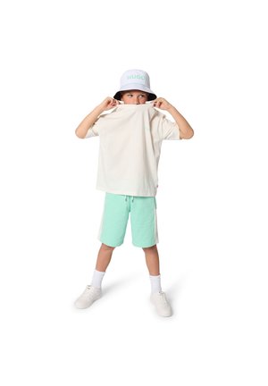 T-shirt en coton blanc avec des accents menthe, associé à un short menthe. L'enfant porte un chapeau seau bleu clair avec le logo "HUGO" en vert.