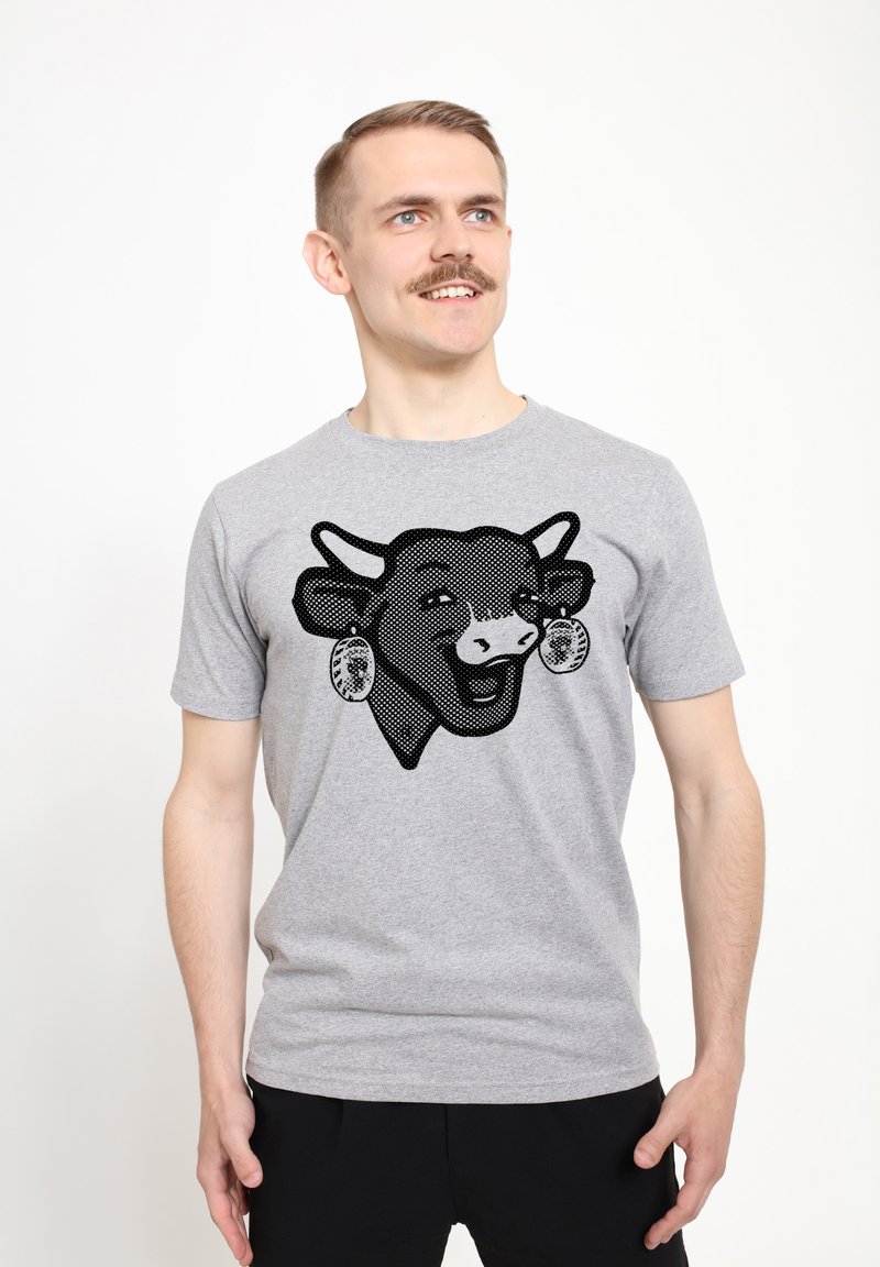 Graues Baumwoll-T-Shirt mit einem schwarzen, gepunkteten Kuh-Graphic, die Ohrringe und einen lächelnden Gesichtsausdruck zeigt. Kurzärmlig mit Rundhalsausschnitt.
