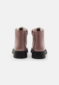 Botas de tobillo de charol rosa con un forro suave, que presentan una lengüeta en la parte posterior y una suela de goma negra gruesa para tracción.