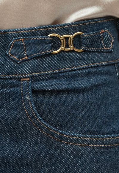 Material din denim albastru închis cu accesorii aurii, prezentând un design distinctiv al buclei de centură și cusături contrastante de-a lungul taliei și buzunarelor.