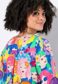 Blusa colorata con un motivo di volti stilizzati dai vari colori di capelli. Realizzata in tessuto leggero con vestibilità ampia e scollatura rotonda.