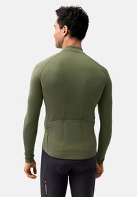 Camiseta de rendimiento verde de manga larga con un diseño ajustado, textura suave y mangas raglán. Cuenta con bolsillos traseros y un acento de cremallera.