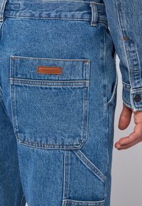 Denim cargo byxor i ljusblå med en strukturerad yta. Funktioner inkluderar flera fickor, orange sömmar och en brun läderetikett från Trussardi.
