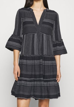 Woman wearing a black dress with white vertical and horizontal stripes, featuring three-quarter bell sleeves and a V-neckline.